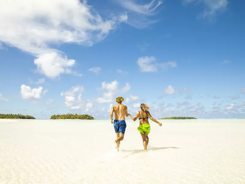 Couple runs through shallow lagoon water infront of islets